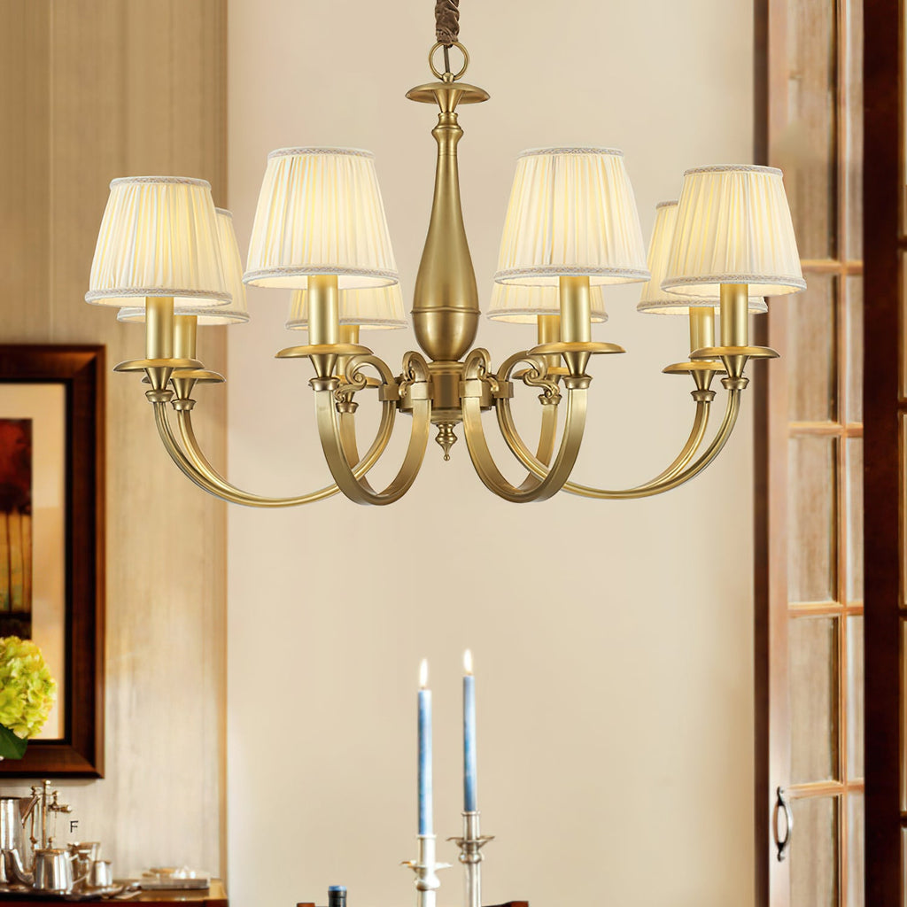 Lit Clérachic brass chandelier in a dining room, above a table set with tall blue candles, a framed picture to the left.