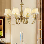 Lit Clérachic brass chandelier in a dining room, above a table set with tall blue candles, a framed picture to the left.