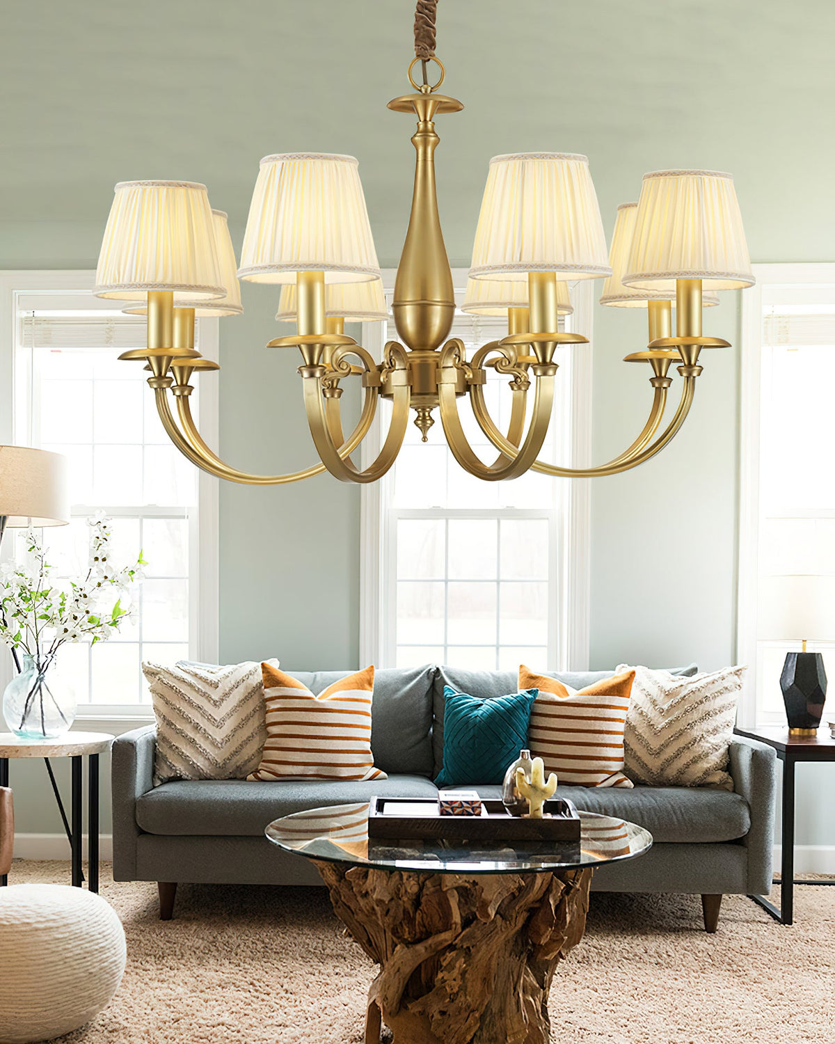 Wider view of a Clérachic chandelier with pleated white shades in a sitting room, above a driftwood-based glass coffee table.