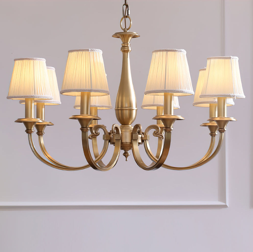This Clérachic brass chandelier with pleated fabric shades hangs against a lilac-grey panelled wall, its antique brass finish glowing.
