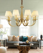 Clérachic chandelier with warm-lit pleated shades over a grey sofa with striped and teal cushions, in a pale green room.