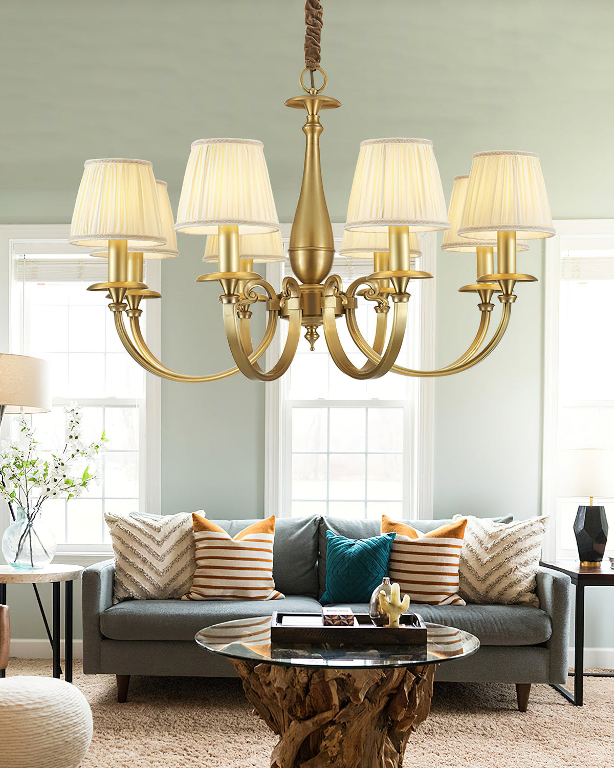 Clérachic chandelier with warm-lit pleated shades over a grey sofa with striped and teal cushions, in a pale green room.
