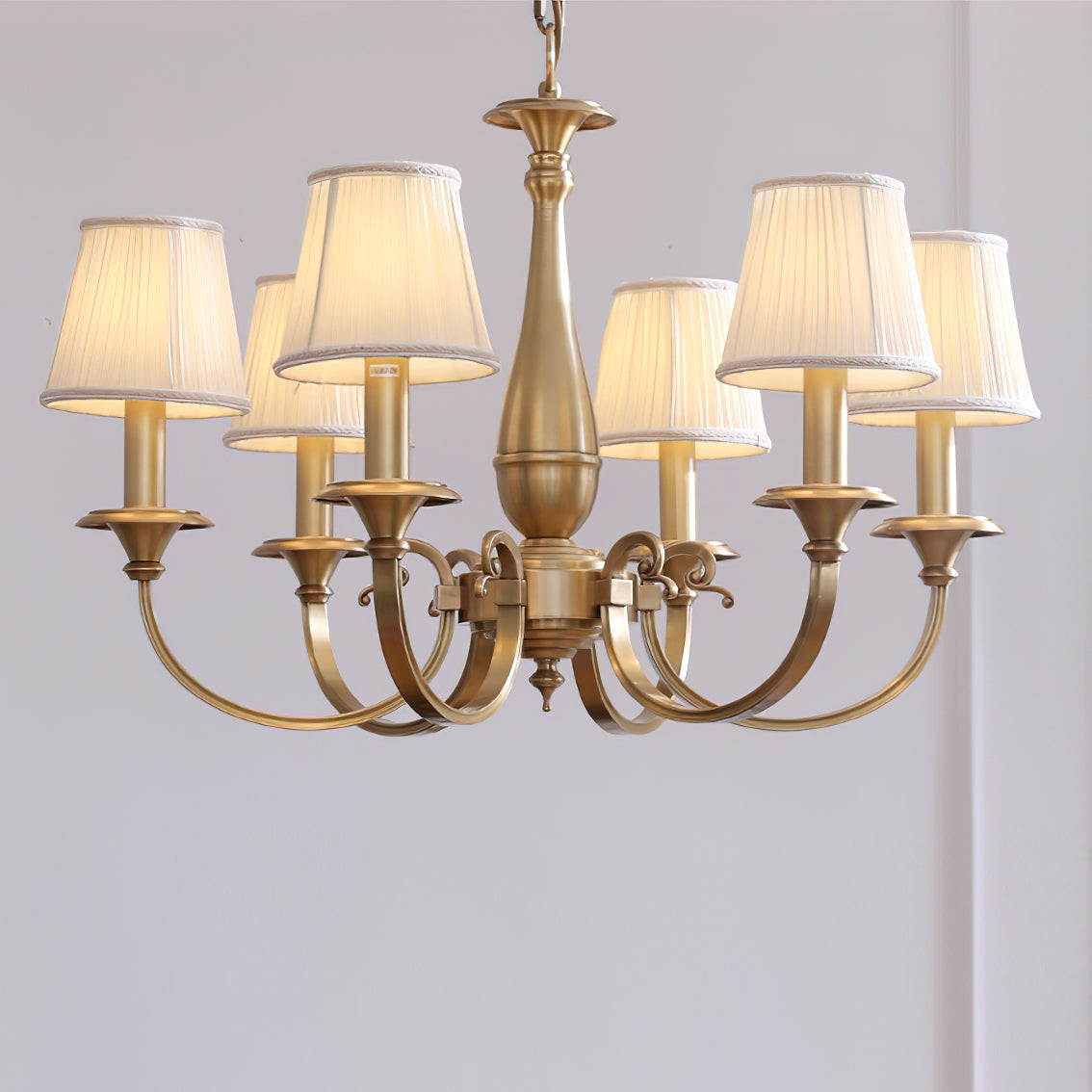 Underside view of this Clérachic brass chandelier, its pleated white shades lit and its brass arms sweeping outward and down.