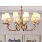 Close view of a Clérachic chandelier with wide brass arms and pleated shades, hung in front of framed architectural prints.