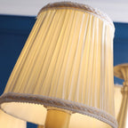 Close view of a pleated white fabric shade with a woven trim edge on this Clérachic chandelier, lit from within.