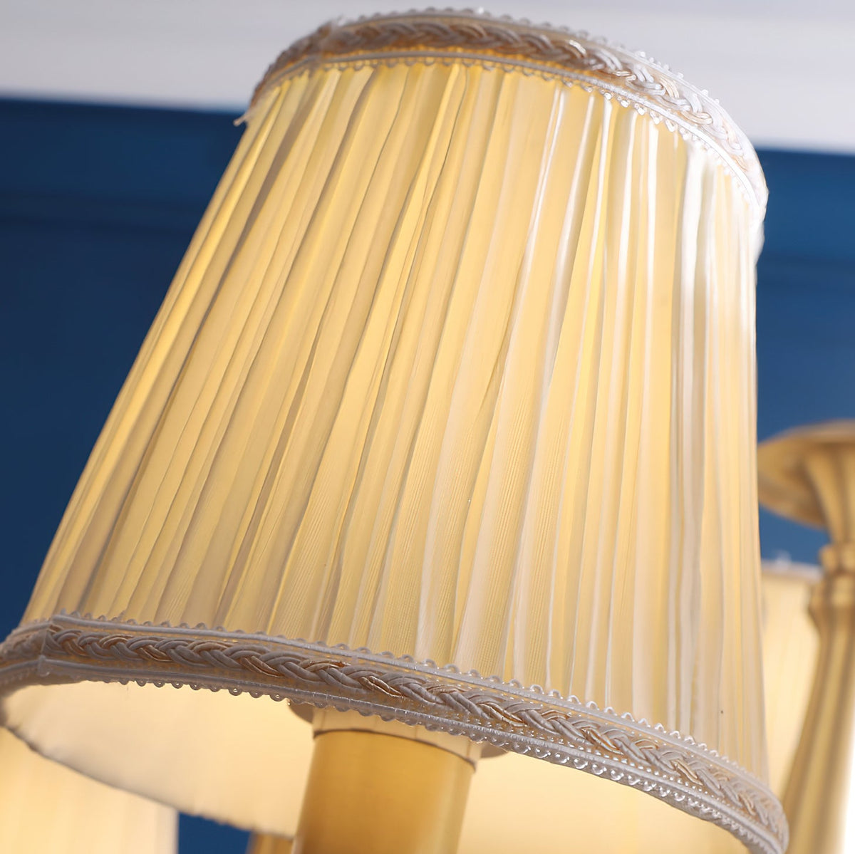 Close view of a pleated white fabric shade with a woven trim edge on this Clérachic chandelier, lit from within.
