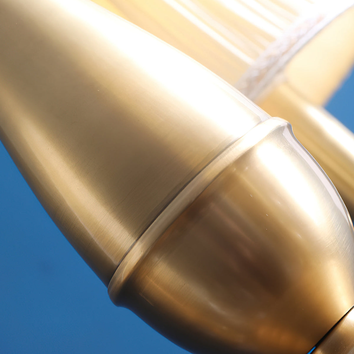 Close view of the smooth brass stem and its rounded collar on this Clérachic chandelier, against a blue backdrop.