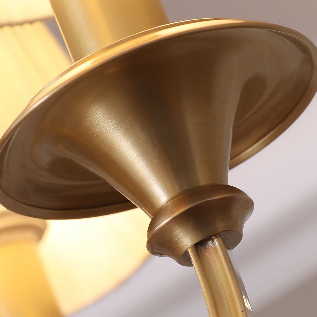 Close view of the flared brass cup beneath a candle holder on this Clérachic chandelier, with a lit shade behind.