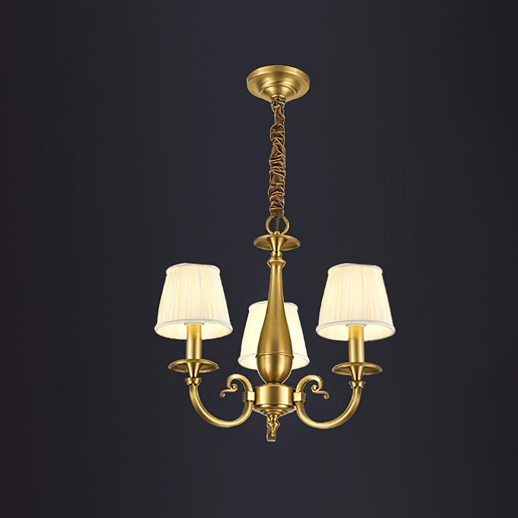 This three-light Clérachic brass chandelier on a dark backdrop, with three pleated shades, scrolling arms and a wrapped chain.