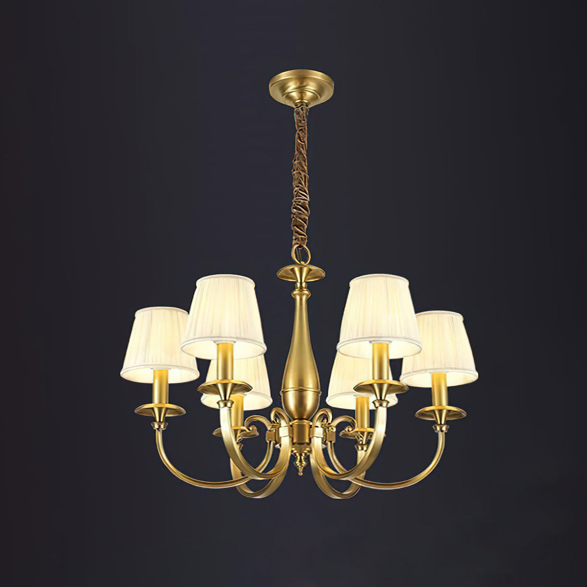 A Clérachic brass chandelier with a six-arm spread on a dark backdrop, pleated white shades lit, hung from a chain.