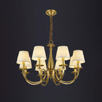 Three-quarter view of this Clérachic brass chandelier with pleated shades and swept brass arms, on a dark backdrop.