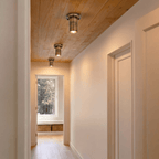 Three vintage brass Clérachic ceiling lights line a wood-paneled hallway leading to a window seat.