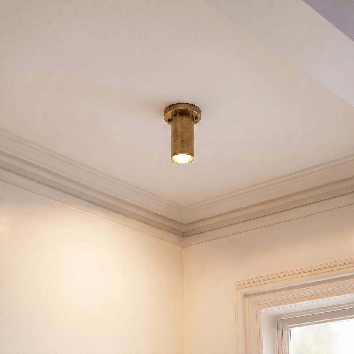 A vintage brass Clérachic ceiling light lights a corner beneath crown molding near a window.