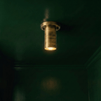 This vintage brass Clérachic ceiling light glows against a dark green wall and matching molding.