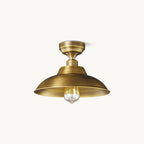 This Clérachic Antique Brass ceiling light on a plain white backdrop, a wide shallow dome shade under a short brass stem with a clear filament bulb.