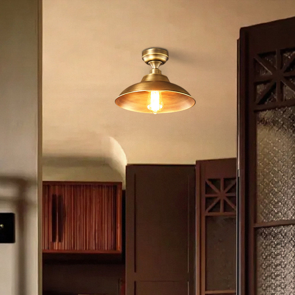 Warm light from a Clérachic brass dome ceiling light above a dark wooden door with a patterned glass panel and a slatted cabinet.