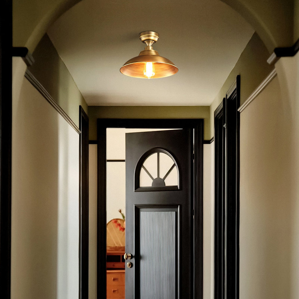 Down a green-walled hallway, a Clérachic brass dome ceiling light glows warm over a black door with a fan-shaped window.