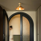 Over black arched double doors with textured glass, a Clérachic brass dome ceiling light lit warm under a dark ceiling.
