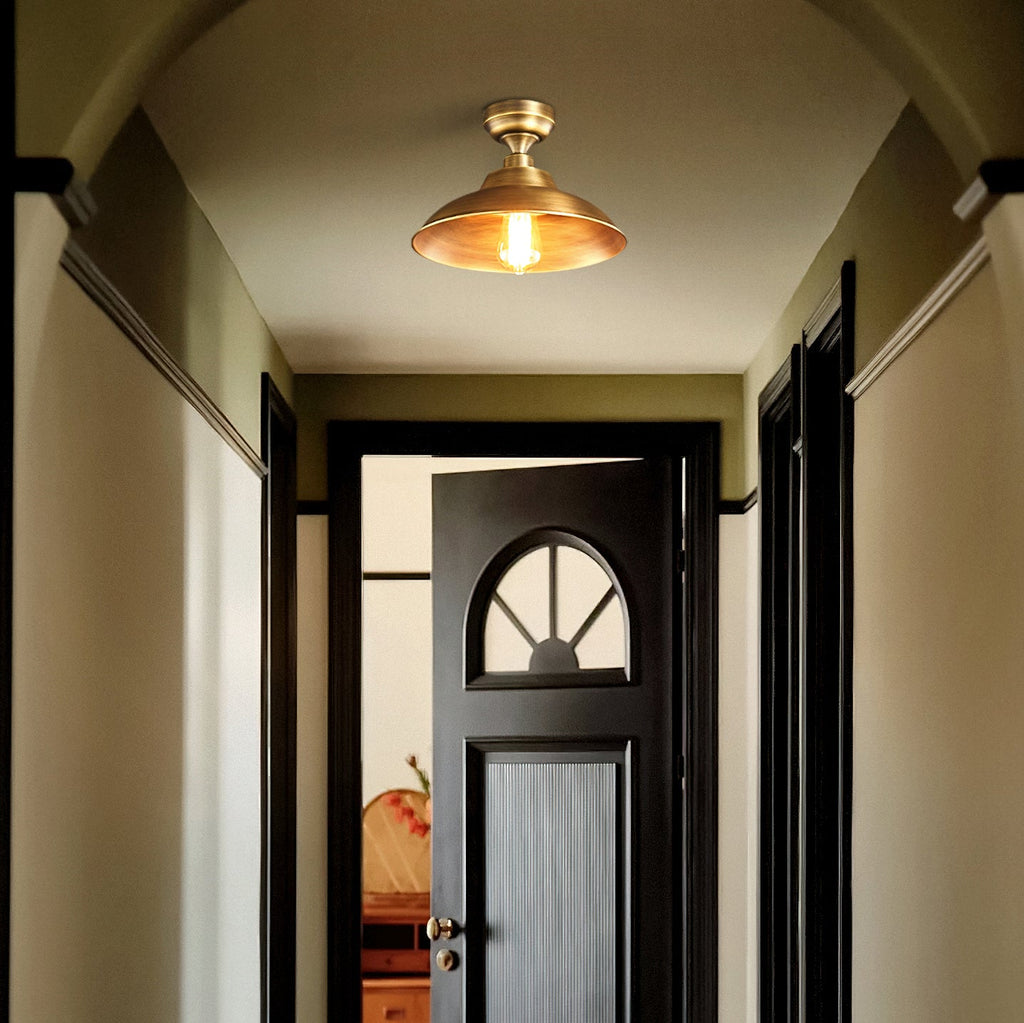 Looking down a hallway toward a half-open black door, this Clérachic brass dome ceiling light is lit warm in the olive-toned space.