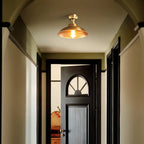 Looking down a hallway toward a half-open black door, this Clérachic brass dome ceiling light is lit warm in the olive-toned space.