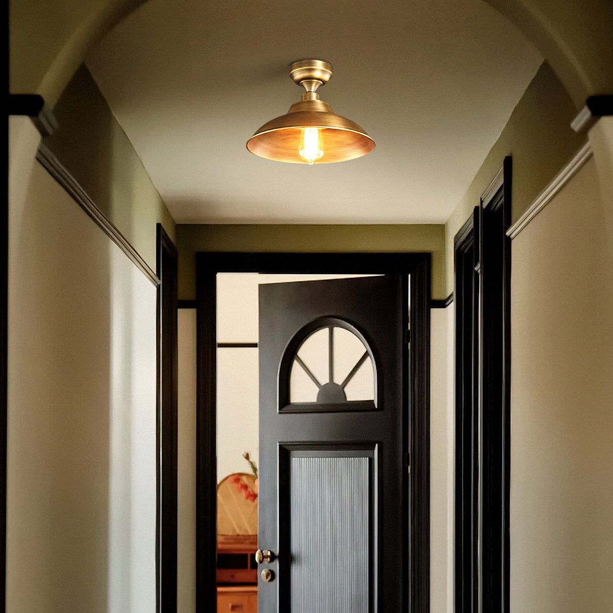 Looking down a hallway toward a half-open black door, this Clérachic brass dome ceiling light is lit warm in the olive-toned space.