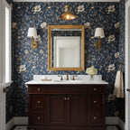 A Clérachic brass dome ceiling light above a washbasin with a gilt mirror and two wall lights, against dark blue floral wallpaper.