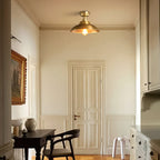 On a cream ceiling above a panelled door and a dark desk with a black chair, a Clérachic brass dome ceiling light stays unlit.