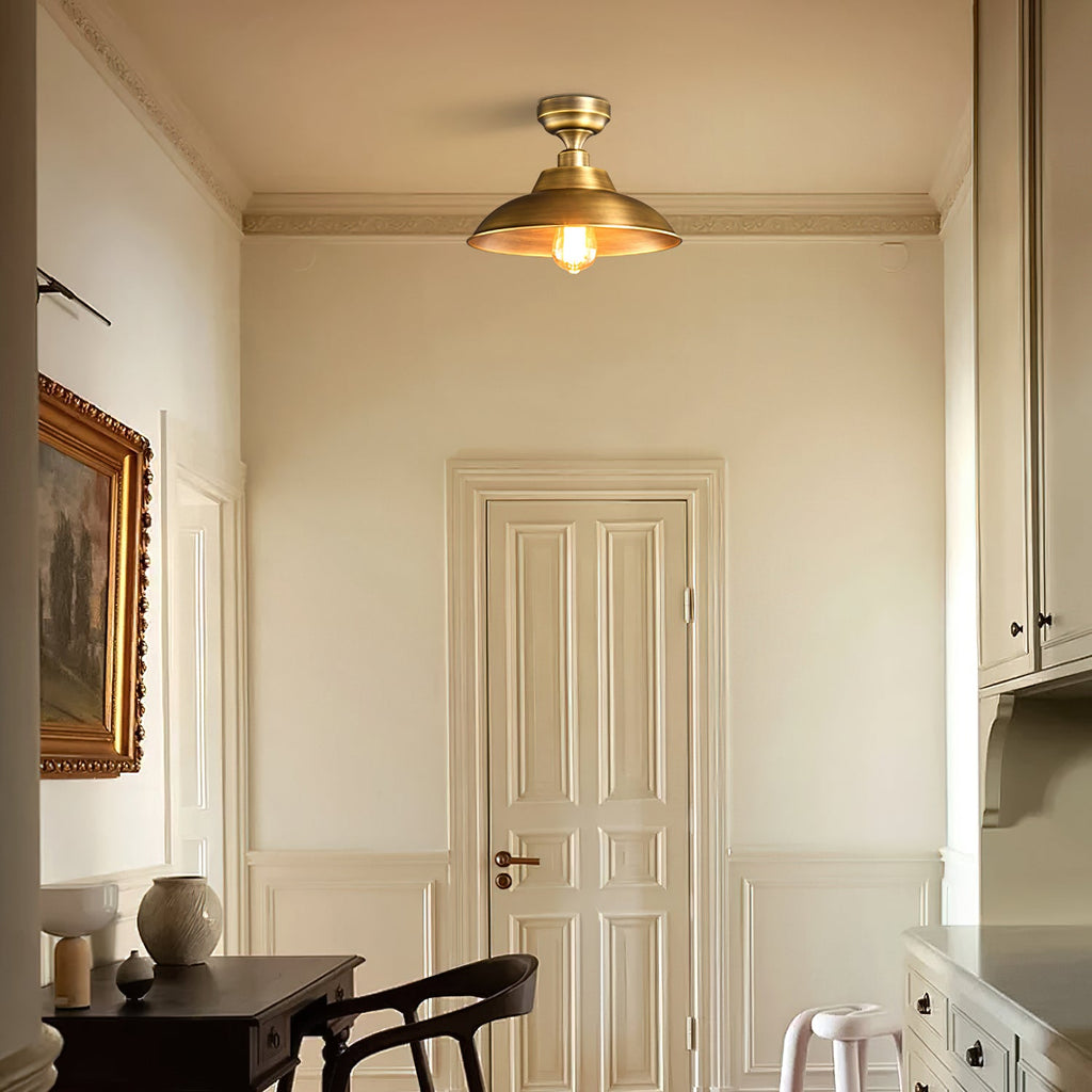 This Clérachic brass dome ceiling light in a cream corridor with a panelled door, a dark desk and a chair seen below.