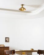 Seen from below, this Clérachic brass dome ceiling light sits flush near a white coved ceiling, above a wall picture and a wooden sideboard.