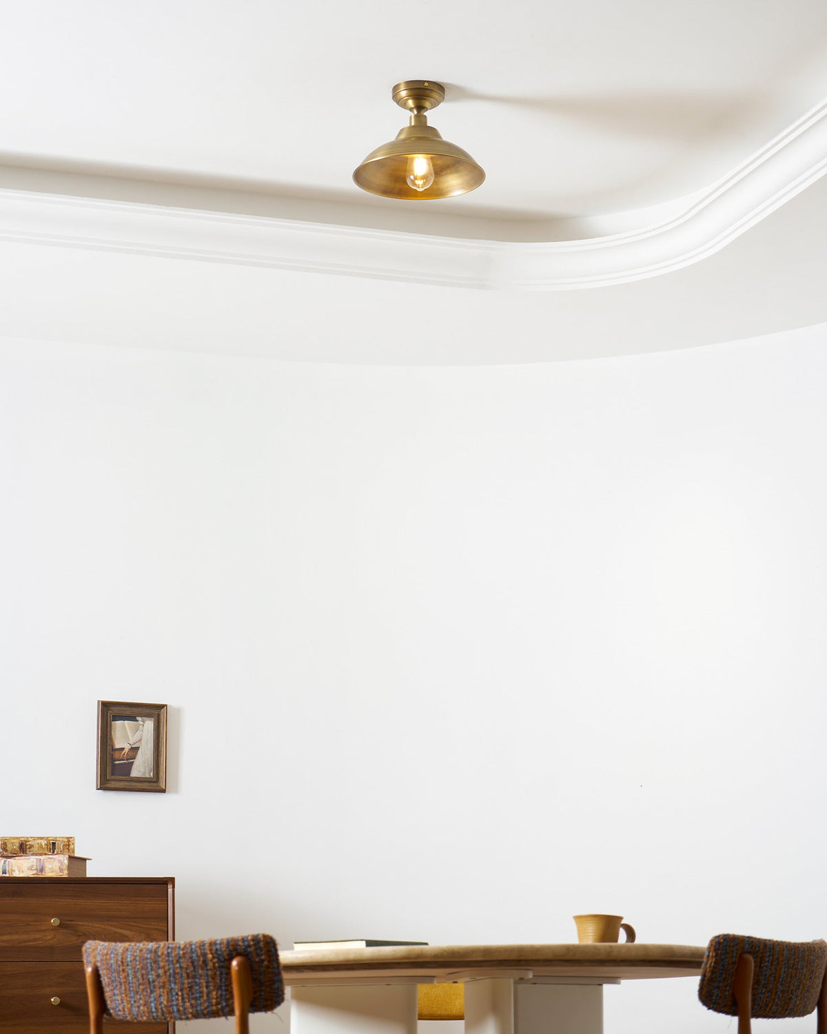 Seen from below, this Clérachic brass dome ceiling light sits flush near a white coved ceiling, above a wall picture and a wooden sideboard.