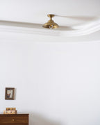 Wide view of a white room and curved ceiling edge, with a Clérachic brass dome light unlit above a wall picture and a walnut sideboard.