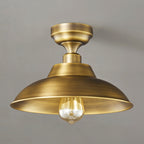 Close view of this Clérachic ceiling light in Antique Brass, with a brushed finish on the dome and a clear bulb on a grey backdrop.