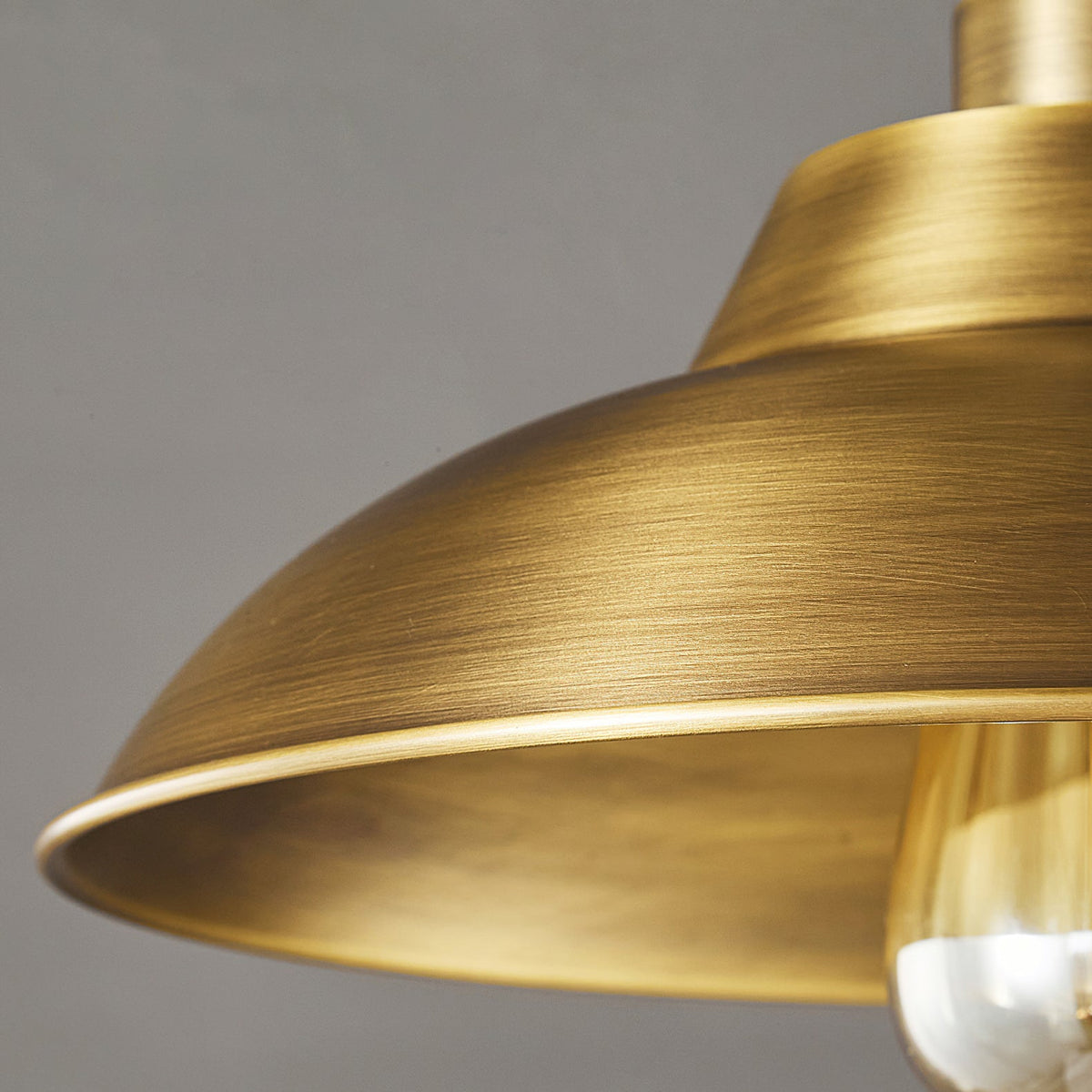 Close detail of the brushed Antique Brass dome and rolled rim on this Clérachic ceiling light, with the clear bulb just in view.