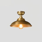 This Clérachic ceiling light in Antique Brass on a pale grey backdrop, a wide shallow dome under a stepped round canopy with a warm bulb.