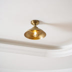 Fitted flush to a white ceiling beside a cornice, this Clérachic brass dome light glows with a warm bulb inside the shade.