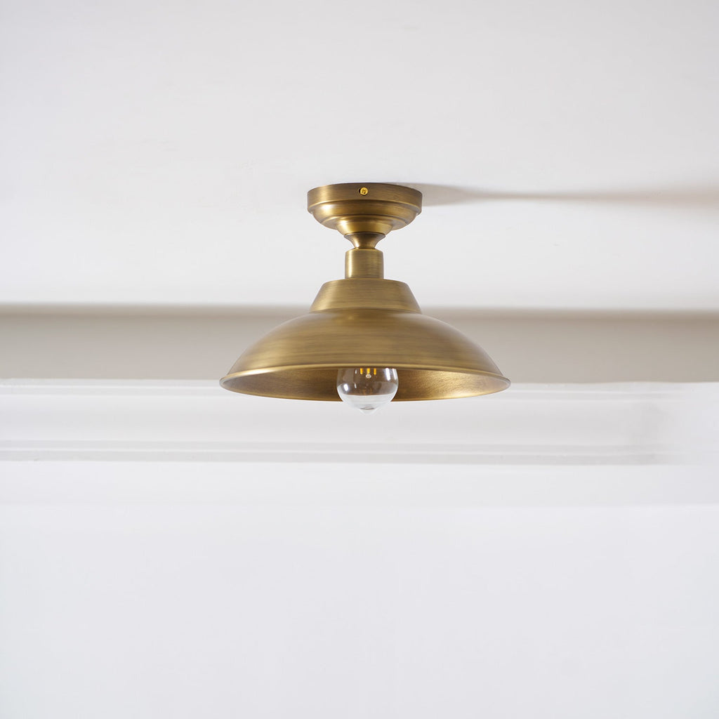 The same Clérachic brass dome ceiling light with a clear bulb that is not lit, shown against a white ceiling and a deep cornice.