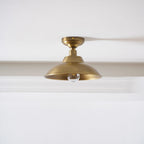 The same Clérachic brass dome ceiling light with a clear bulb that is not lit, shown against a white ceiling and a deep cornice.