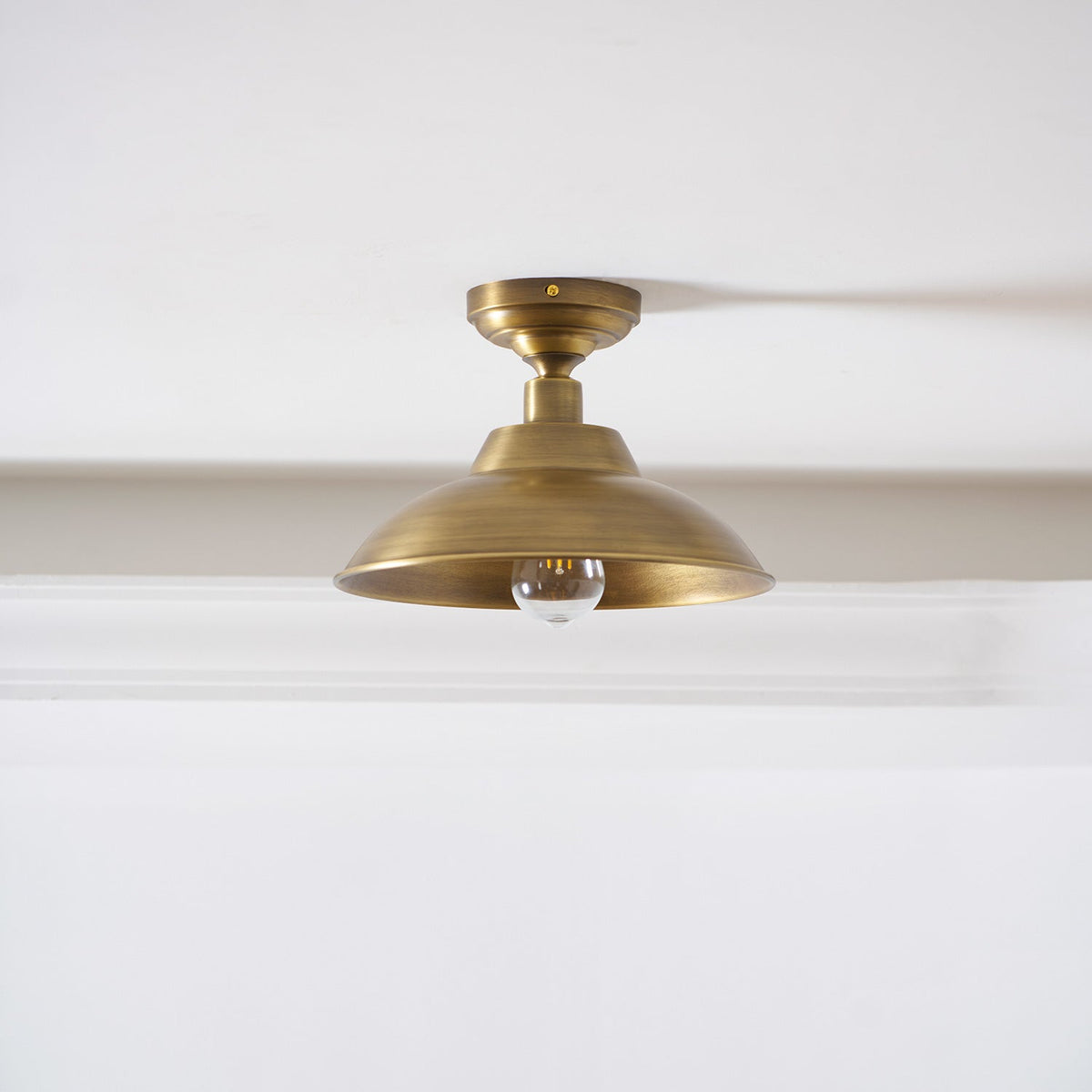 The same Clérachic brass dome ceiling light with a clear bulb that is not lit, shown against a white ceiling and a deep cornice.