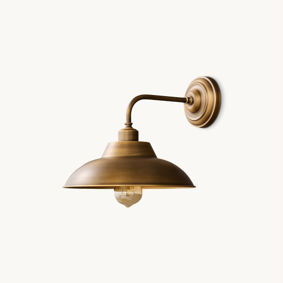 This Clérachic antique brass wall light has a round dome shade on a curved arm and a bare bulb, shown on a plain white backdrop.