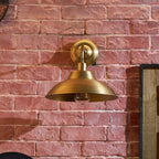 Front view of this Clérachic brass dome wall light against a rough red brick wall, with a wooden panel at the edge of the frame.