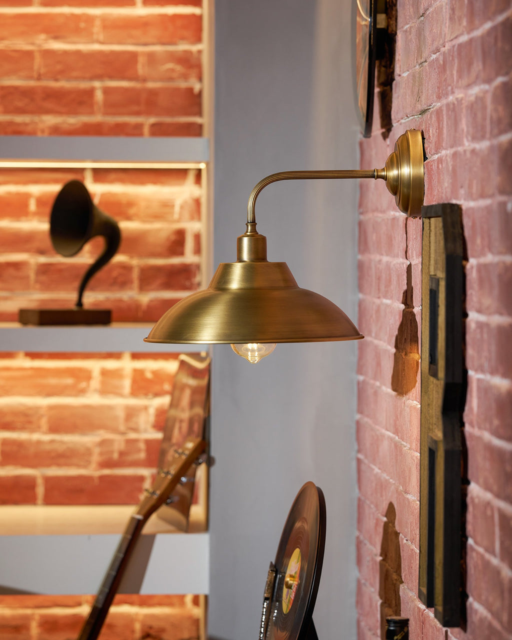 From the side, this Clérachic brass wall light reaches out from a brick wall beside shelves holding a gramophone horn and records.