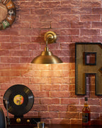 Glowing warmly on a brick wall, this Clérachic brass wall light sits beside a large wooden letter R and a vinyl record on a sideboard.