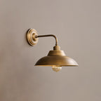 Side view of this Clérachic antique brass wall light on a soft taupe wall, with a clear bulb hanging below the dome shade.