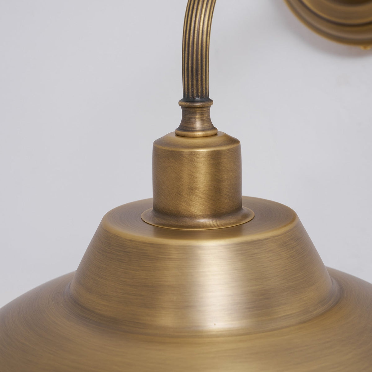Close view of the brushed brass finish, fluted arm and collar where it joins the dome shade on this Clérachic wall light.