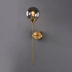 Clérachic Brass-Finish Globe Wall Sconce in smoke gray glass, lit against a soft grey wall with the brass stem running past the round plate.