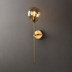 The amber glass option of the Clérachic Brass-Finish Globe Wall Sconce, glowing honey above its brushed brass stem on a warm grey wall.