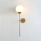 Milk white glass on the Clérachic Brass-Finish Globe Wall Sconce, an even soft glow against a bare white plaster wall.