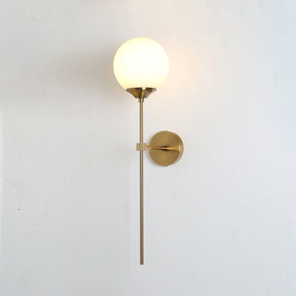 Milk white glass on the Clérachic Brass-Finish Globe Wall Sconce, an even soft glow against a bare white plaster wall.