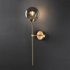 Clérachic Brass-Finish Globe Wall Sconce lit on a charcoal wall, throwing a warm halo behind the smoke gray globe.