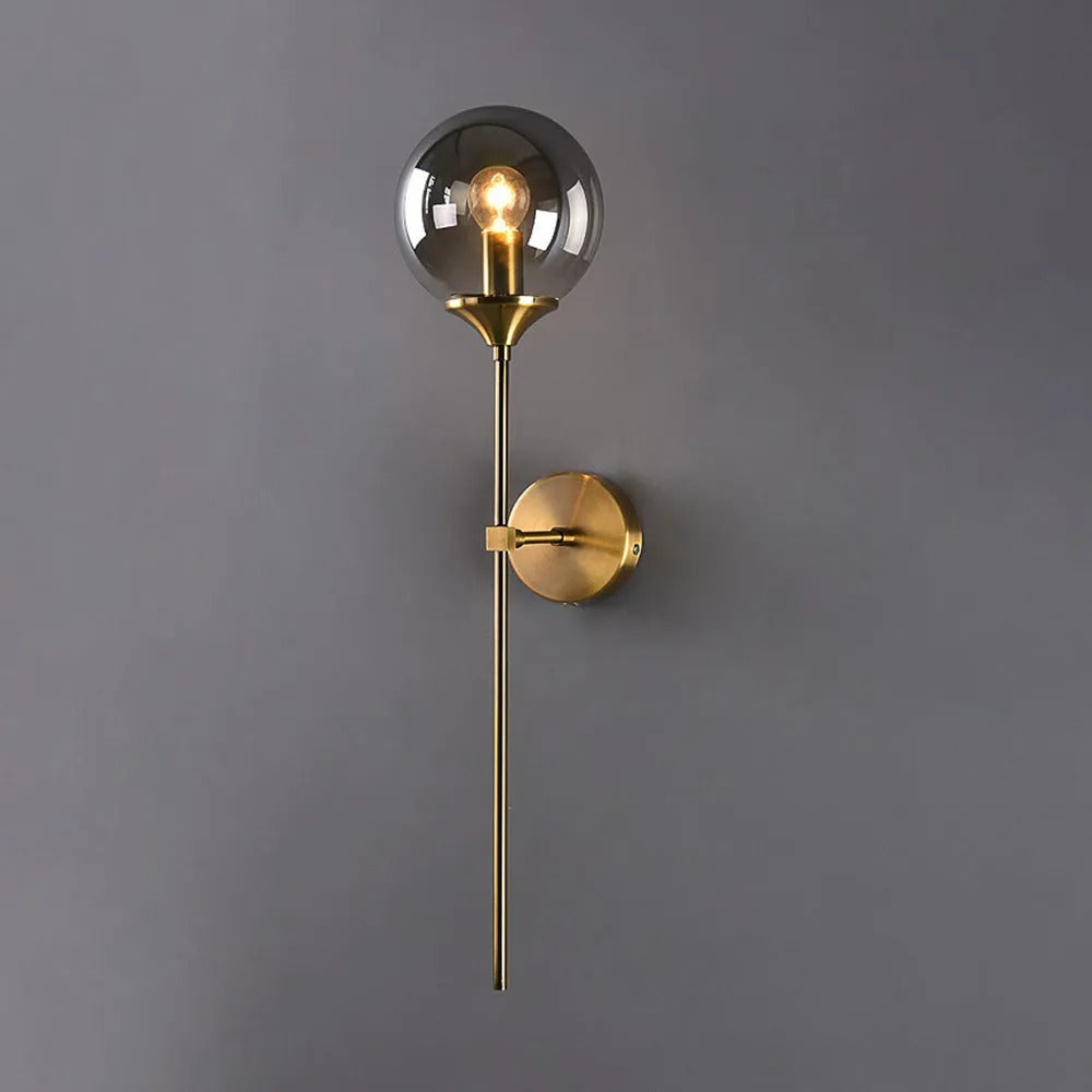 Full-length view of the Clérachic Brass-Finish Globe Wall Sconce, the brass tail dropping well below the fixing point on a grey wall.